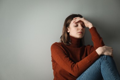 Photo of Sad young woman near grey wall, space for text