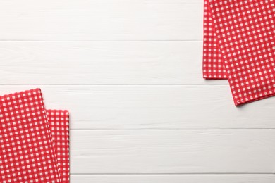 Photo of Red checkered tablecloths on white wooden table, flat lay. Space for text