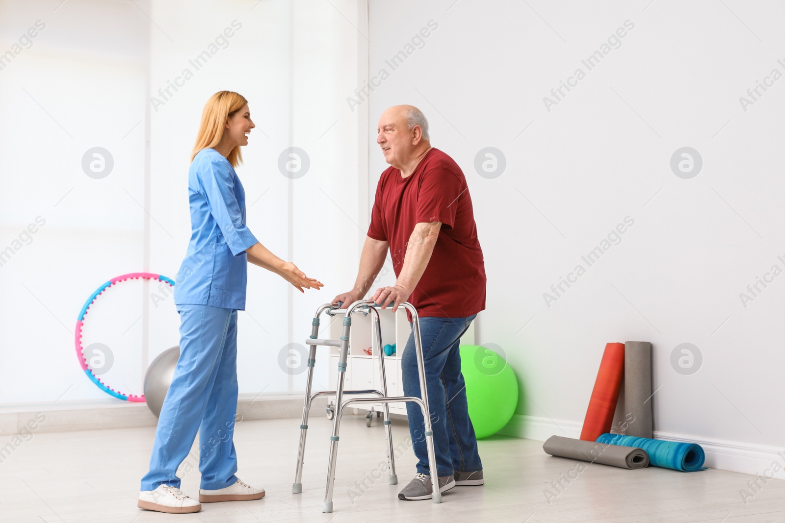 Photo of Caretaker helping elderly man with walking frame indoors