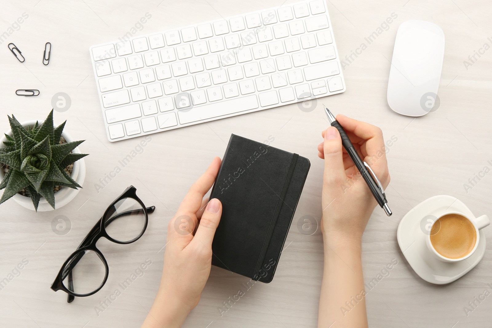 Photo of Woman with notebook and pen at light wooden table, top view