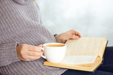 Photo of Woman with cup of coffee reading book at home, closeup