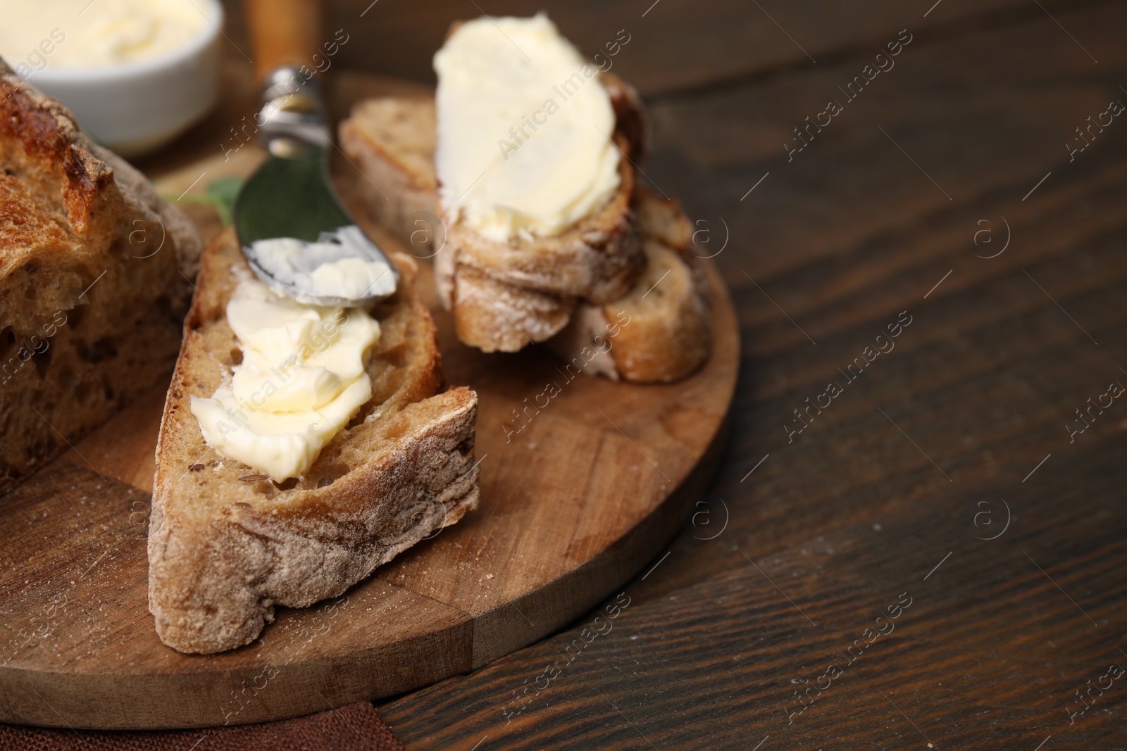 Photo of Tasty bread with butter and knife on wooden table, closeup. Space for text