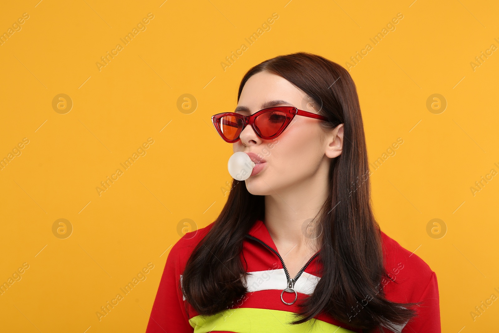 Photo of Beautiful woman in sunglasses blowing bubble gum on orange background, space for text