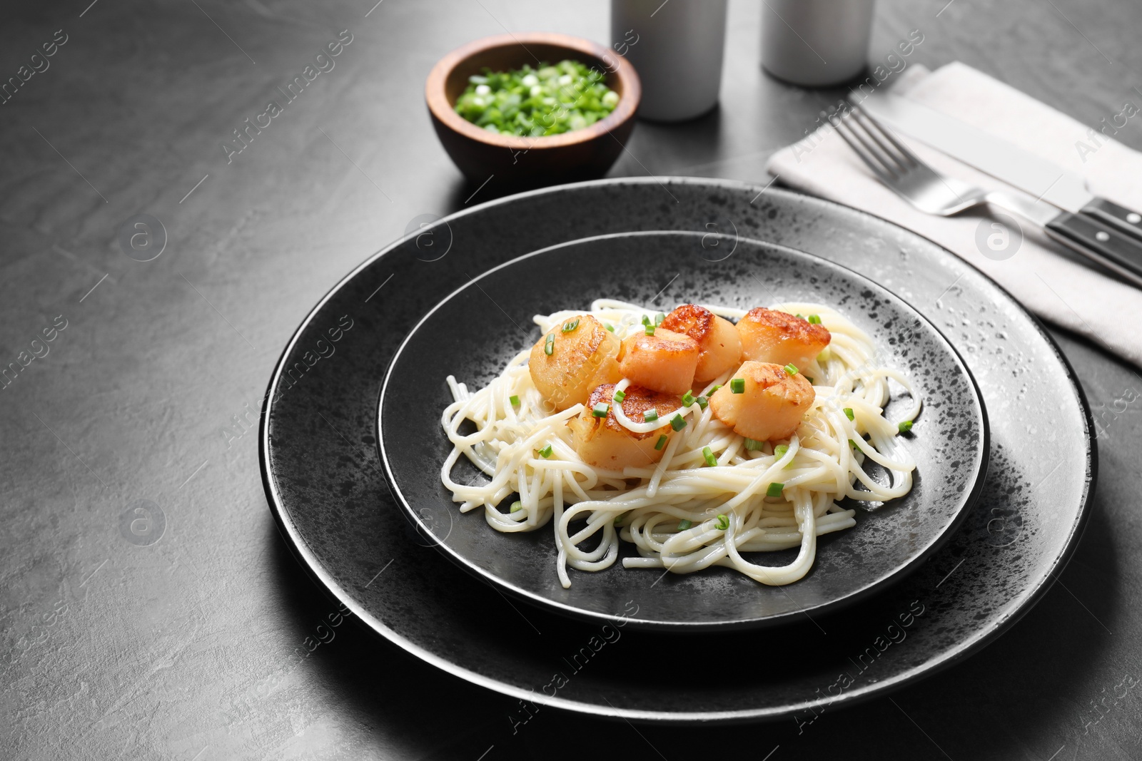 Photo of Delicious scallop pasta with green onion served on grey table