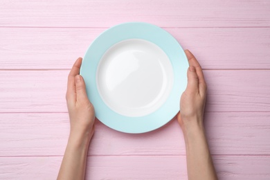 Woman with empty plate at wooden table, top view