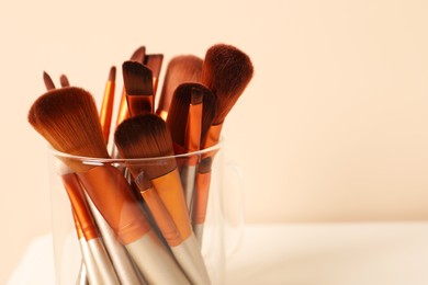 Photo of Set of professional makeup brushes on white table against beige background. Space for text