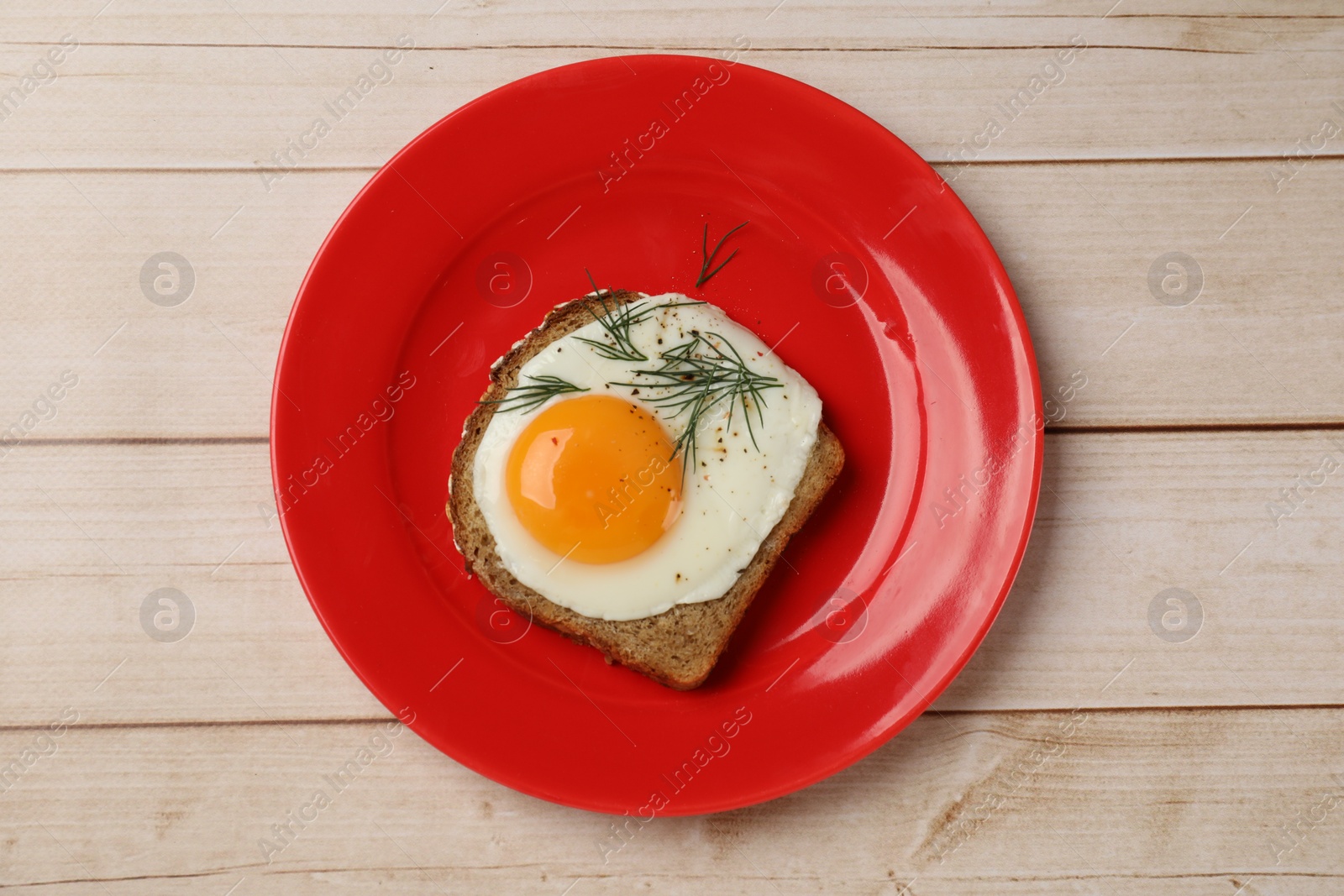 Photo of Plate with tasty fried egg, slice of bread and dill on light wooden table, top view