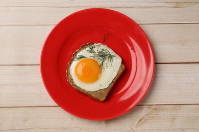 Plate with tasty fried egg, slice of bread and dill on light wooden table, top view