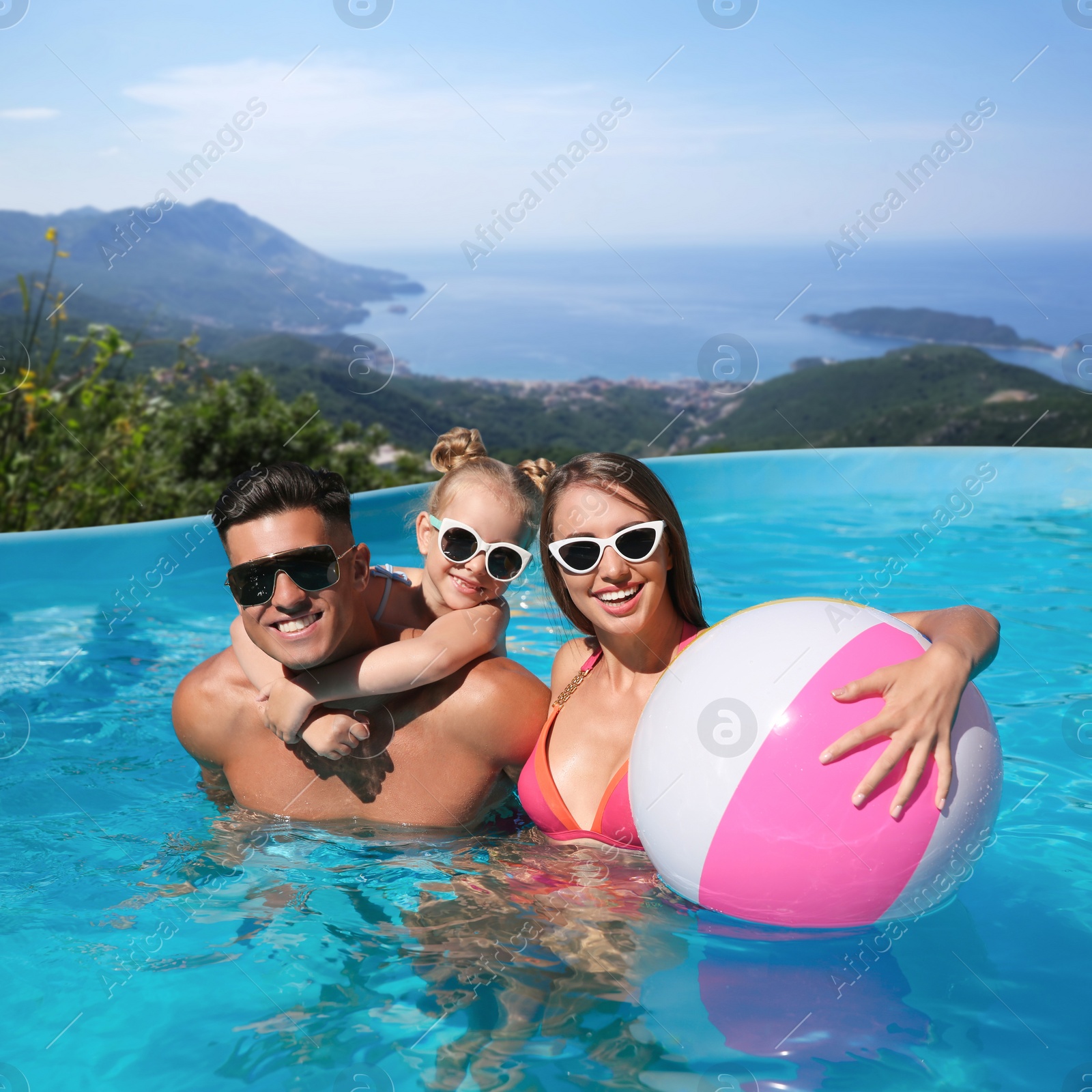 Image of Happy family with inflatable ball in outdoor swimming pool at luxury resort and beautiful view of mountains on sunny day