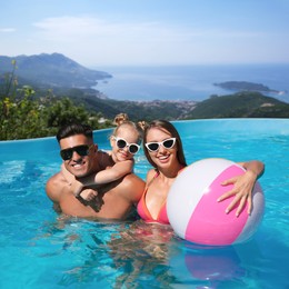 Happy family with inflatable ball in outdoor swimming pool at luxury resort and beautiful view of mountains on sunny day