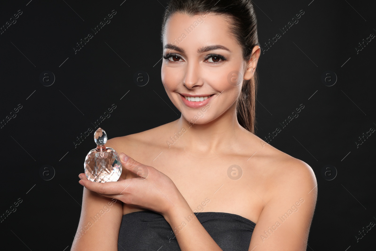 Photo of Young woman with bottle of perfume on black background