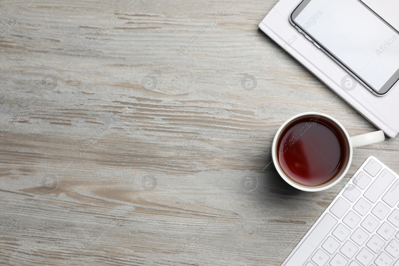 Ceramic mug of aromatic tea, keyboard, book and smartphone on white wooden table, flat lay. Space for text Photo of Ceramic mug of aromatic tea, keyboard, book and smartphone on white wooden table, flat lay. Space for text
