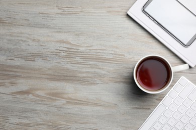 Photo of Ceramic mug of aromatic tea, keyboard, book and smartphone on white wooden table, flat lay. Space for text