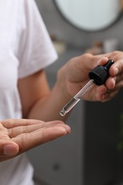 Photo of Woman applying cosmetic serum onto her finger on blurred background, closeup
