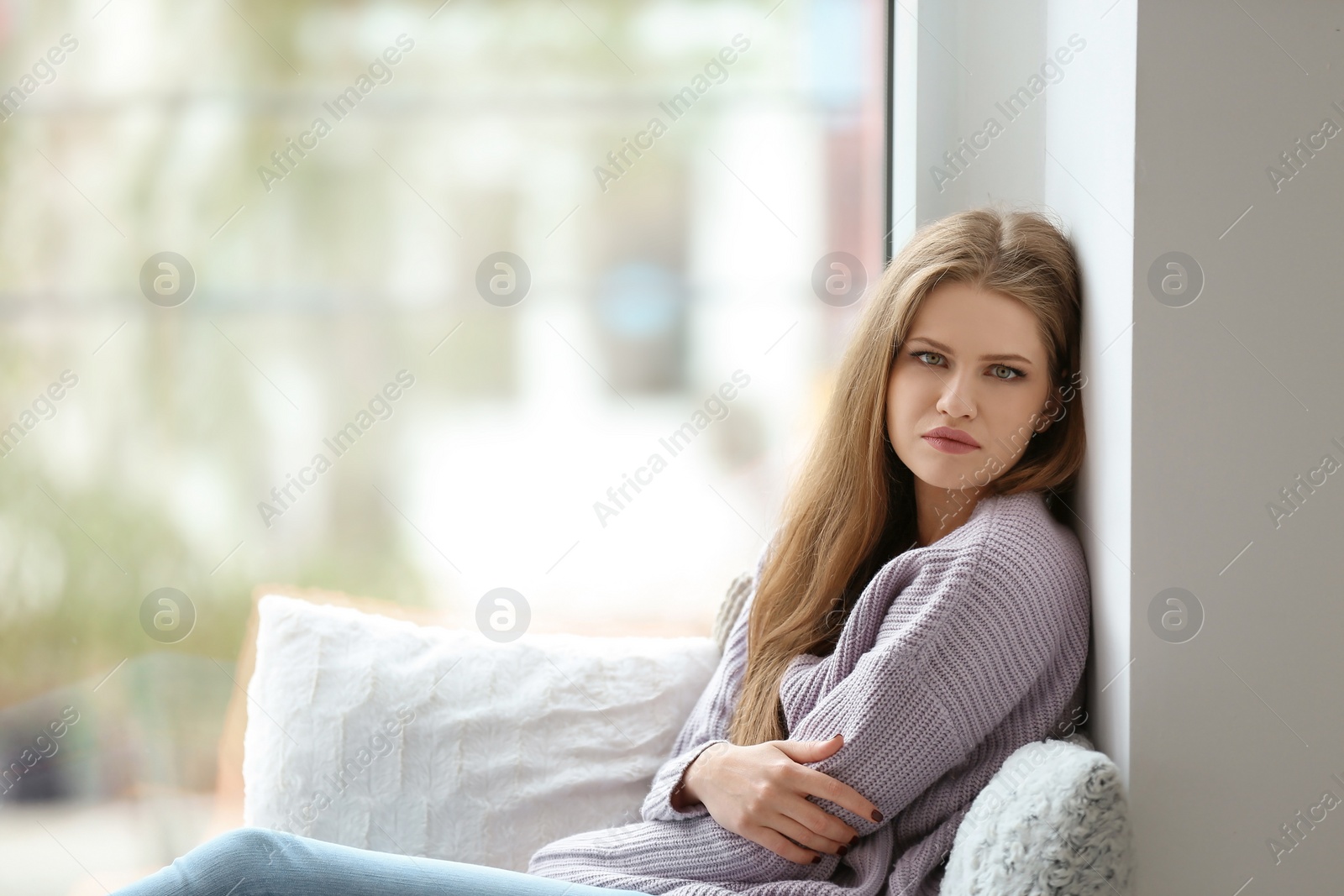Photo of Young sad woman sitting near window at home