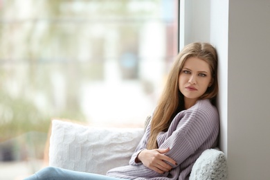 Young sad woman sitting near window at home