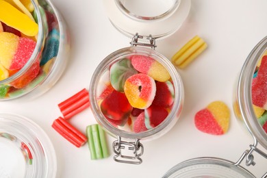 Photo of Tasty jelly candies in jars on white table, flat lay