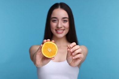 Photo of Beautiful young woman with vitamin pill and piece of orange on light blue background, selective focus