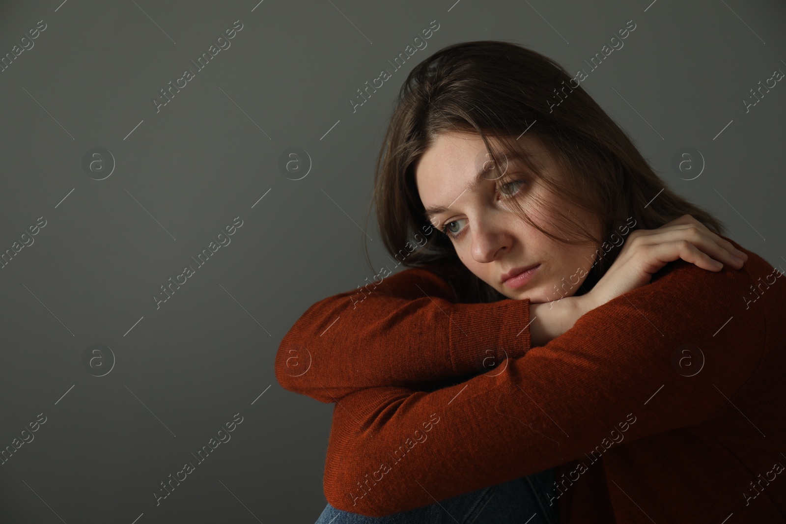 Photo of Sad young woman near grey wall indoors, space for text