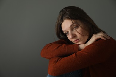 Sad young woman near grey wall indoors, space for text