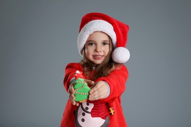 Cute little girl with Christmas gingerbread cookie on grey background