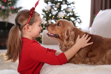 Photo of Cute little girl with English Cocker Spaniel in room decorated for Christmas