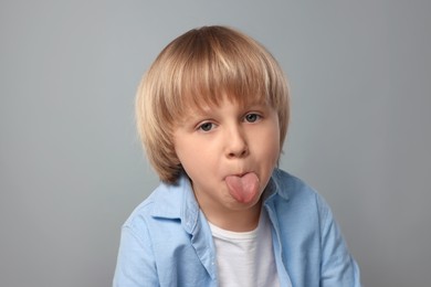 Photo of Cute little boy showing his tongue on grey background