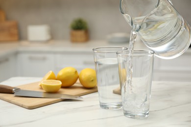 Photo of Pouring water from jug into glass on white table in kitchen, closeup