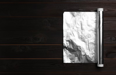 Photo of Roll of aluminum foil on dark wooden table, top view. Space for text