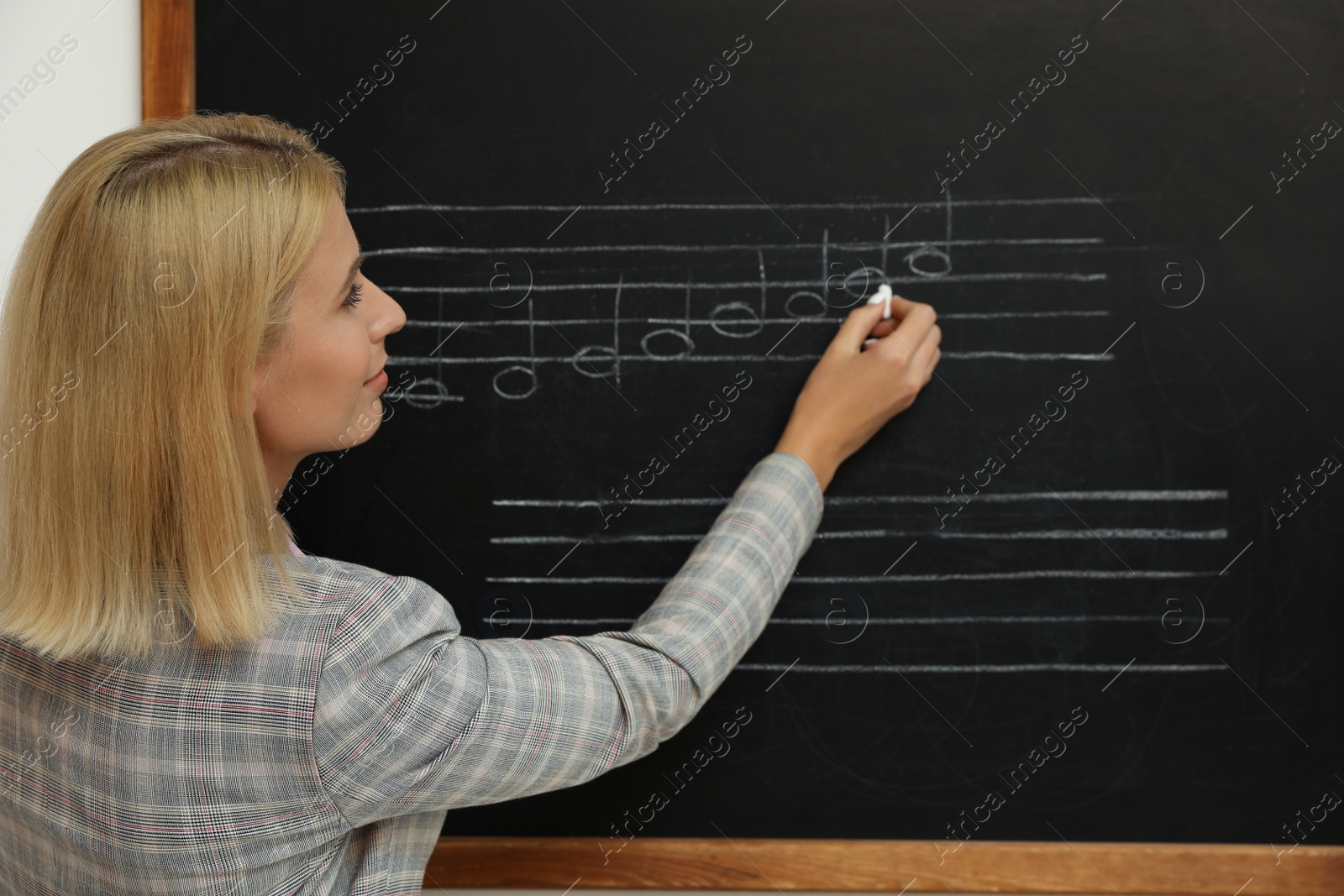 Photo of Teacher writing music notes with chalk on blackboard in classroom