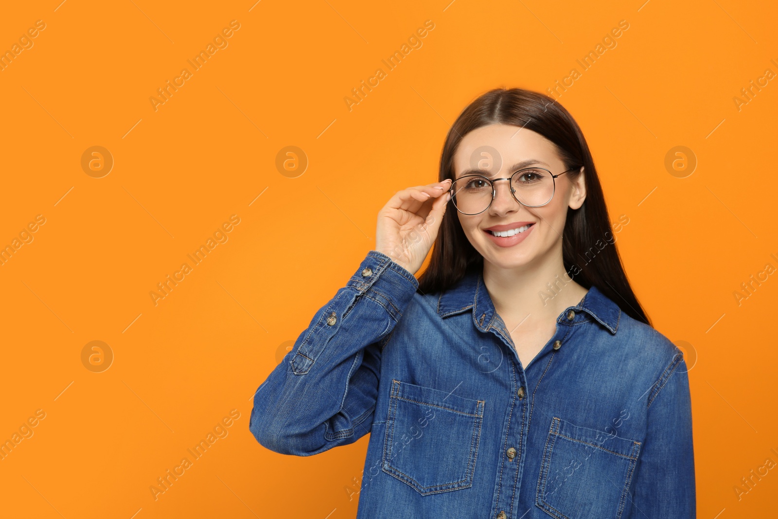 Photo of Portrait of smiling woman in stylish eyeglasses on orange background. Space for text