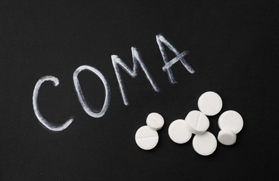 Photo of Pills and word Coma written on black background, flat lay