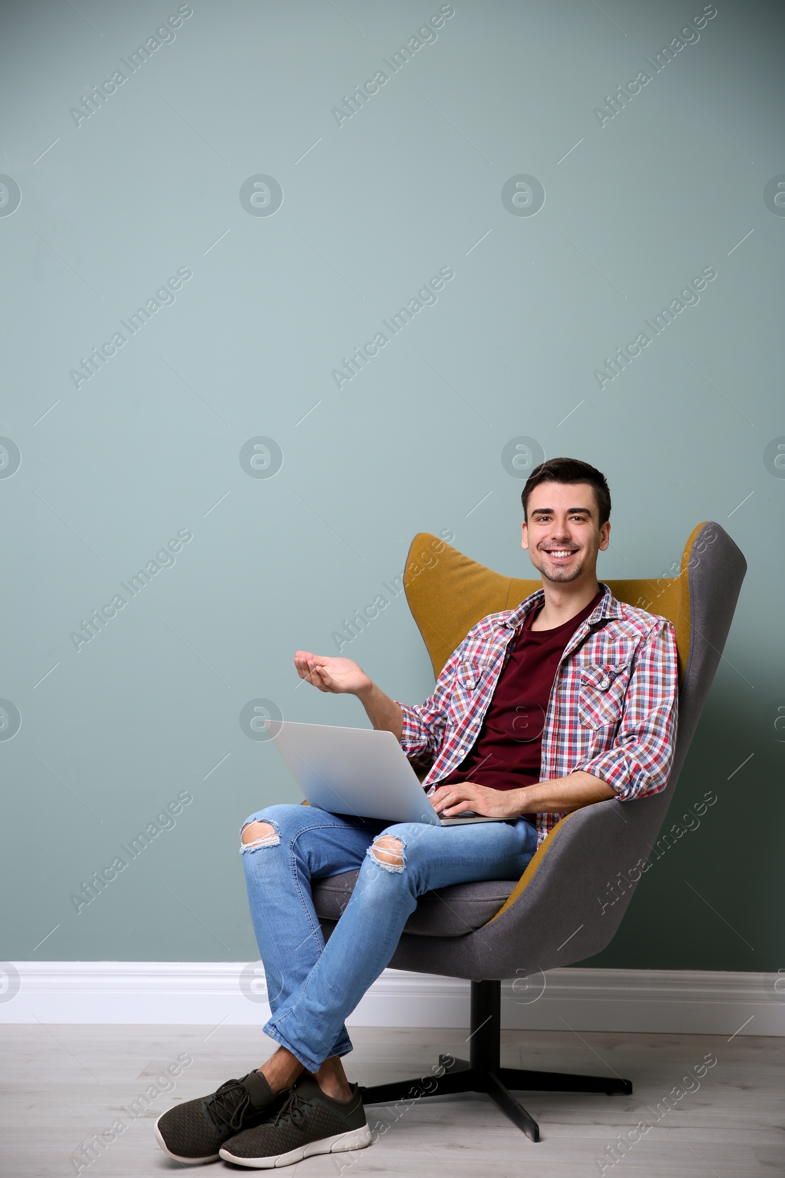 Photo of Young blogger with laptop sitting in armchair against color wall
