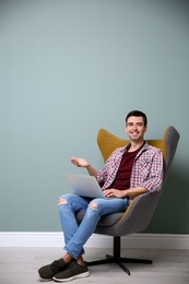 Young blogger with laptop sitting in armchair against color wall