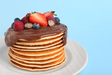 Photo of Stack of tasty pancakes with fresh berries and chocolate spread on light blue background, closeup. Space for text