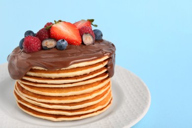 Stack of tasty pancakes with fresh berries and chocolate spread on light blue background, closeup. Space for text