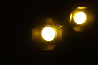 Photo of Bright yellow spotlights near brick wall in darkness, space for text