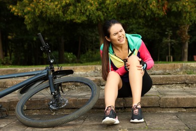 Photo of Young woman with injured knee on steps near bicycle outdoors