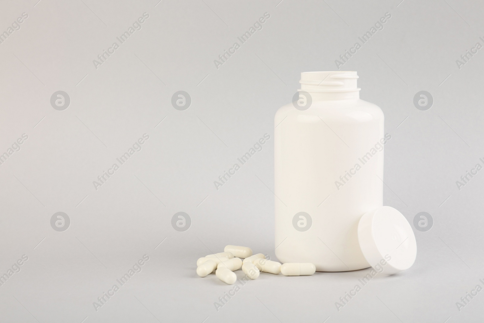 Photo of Blank white jar with vitamin capsules on light grey background, space for text