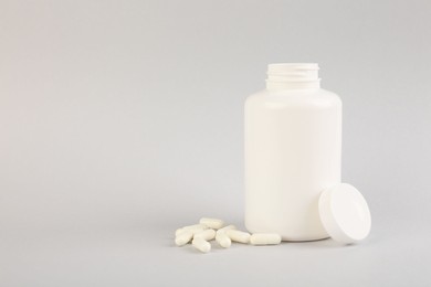 Photo of Blank white jar with vitamin capsules on light grey background, space for text