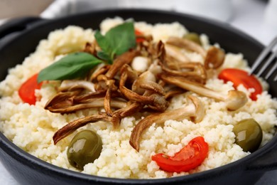 Tasty couscous with mushrooms, olives and tomatoes on table, closeup