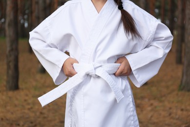Photo of Cute little girl in kimono in forest, closeup. Karate practicing
