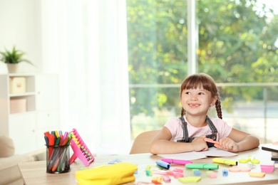 Photo of Cute girl doing homework at table with school stationery indoors