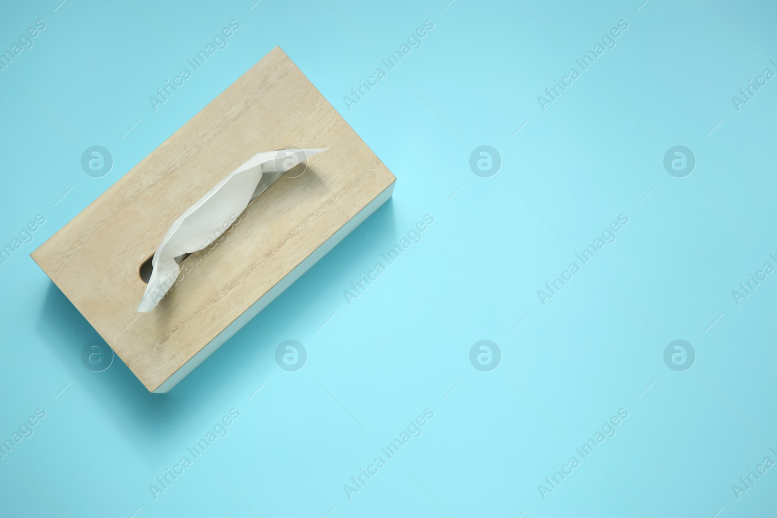 Photo of Wooden holder with paper tissues on light blue background, top view. Space for text