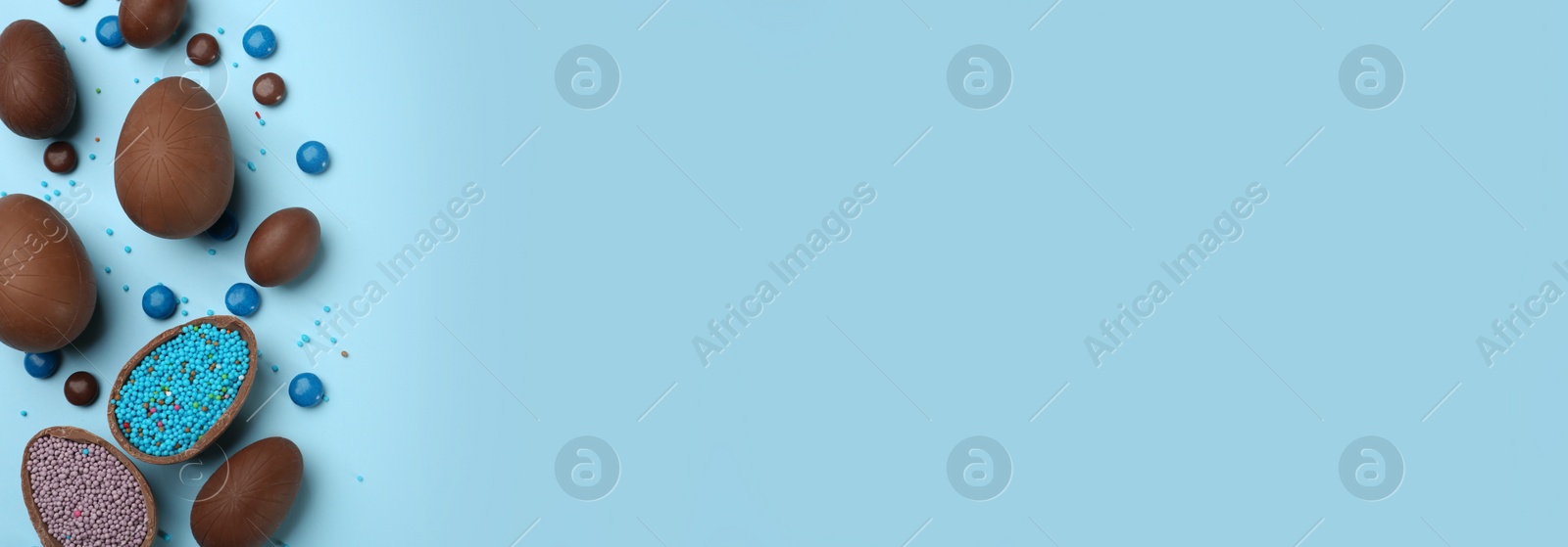 Image of Sweet chocolate eggs on light blue background, flat lay with space for text. Banner design