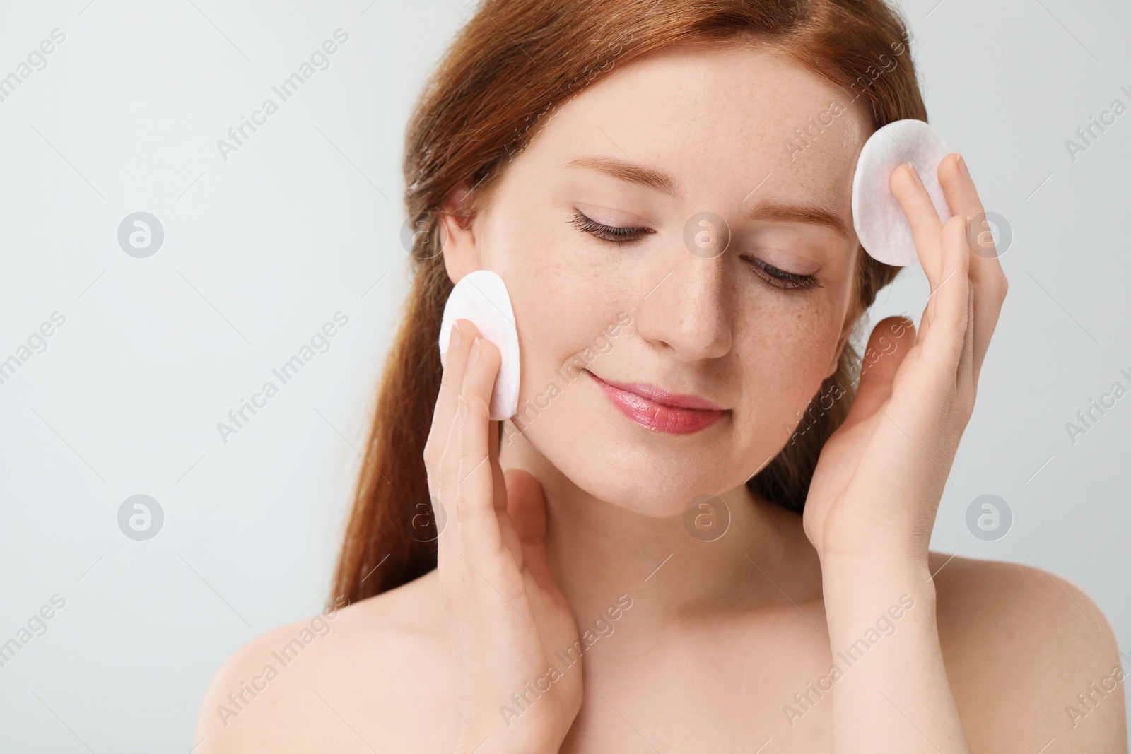 Photo of Beautiful woman with freckles wiping face on grey background