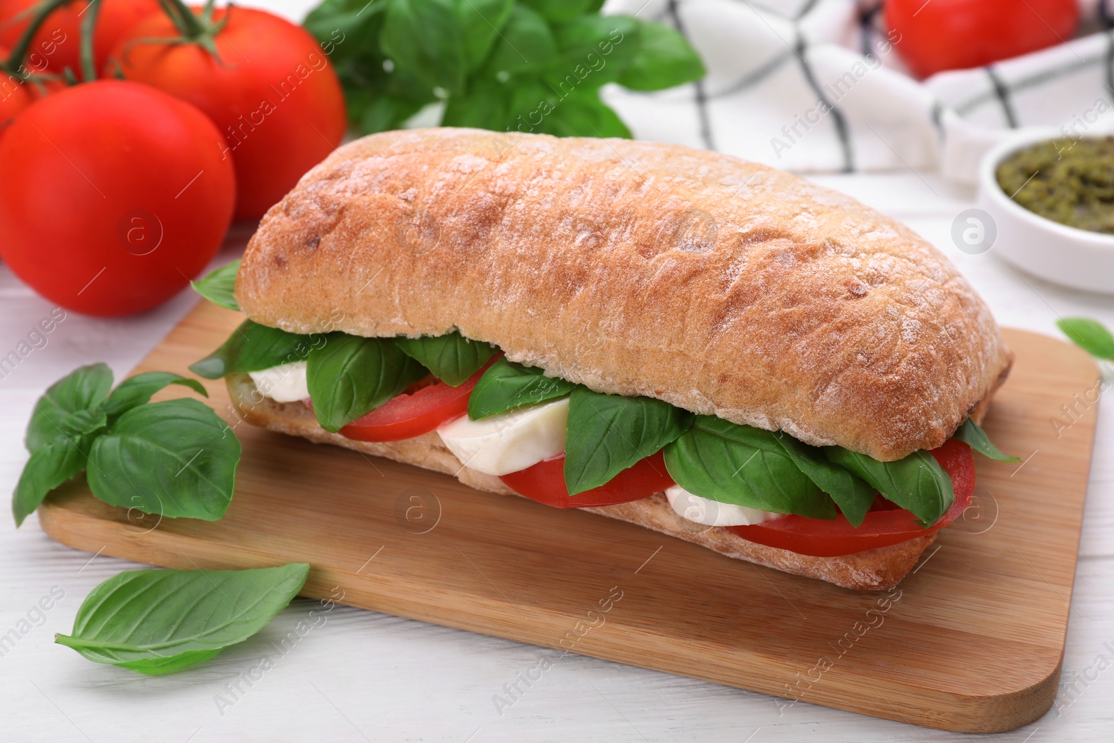 Photo of Delicious Caprese sandwich with mozzarella, tomatoes and basil on white wooden table, closeup