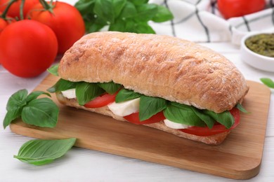 Photo of Delicious Caprese sandwich with mozzarella, tomatoes and basil on white wooden table, closeup