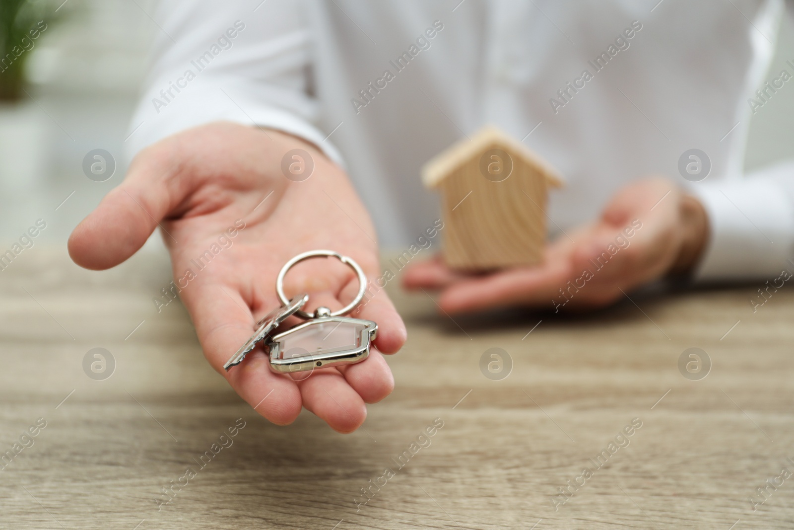 Photo of Real estate agent holding house key with trinket at wooden table, closeup