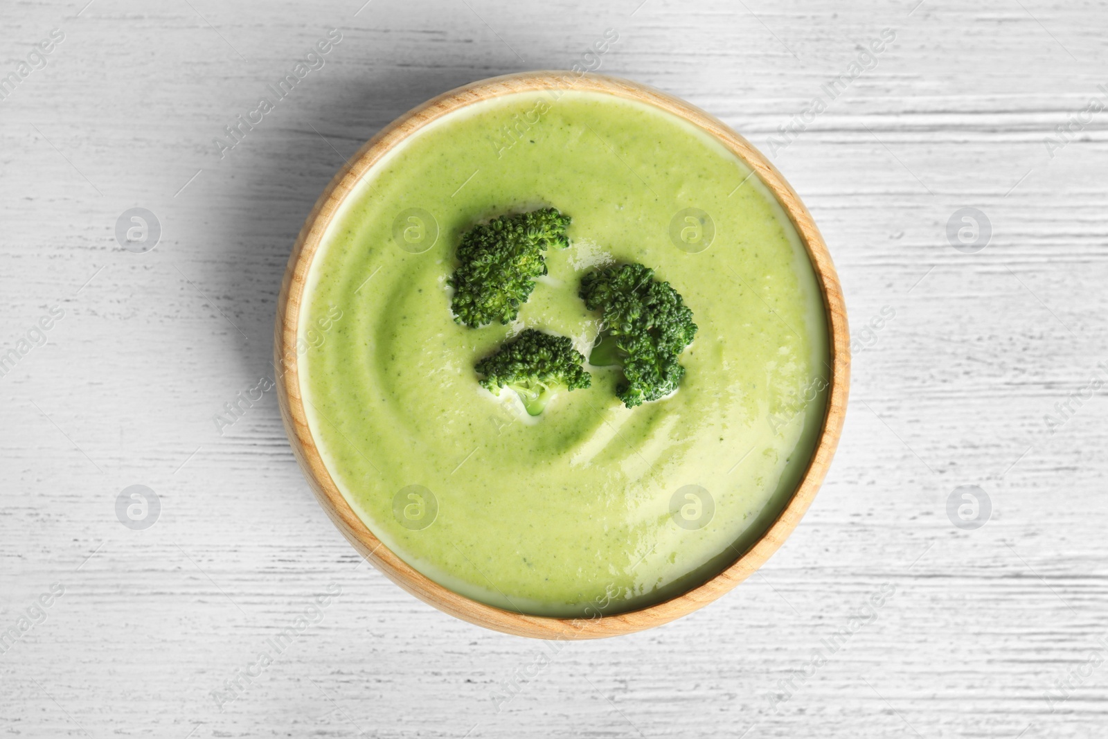 Photo of Delicious broccoli cream soup served on white wooden table, top view